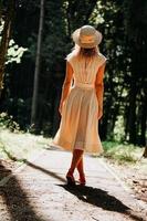 A young woman in a white dress and a straw hat walks through the woods photo