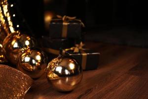 Black gift box with golden ribbon and big gold New Year balls on black