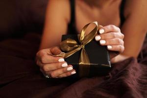 The woman opens a gift in a black box with a gold ribbon photo