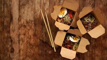 Chinese noodles with chicken in cardboard boxes on a wooden background photo