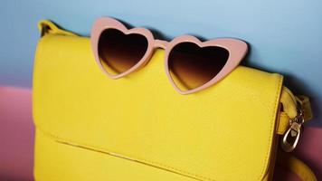 bolso amarillo y gafas de sol en forma de corazón sobre fondo rosa y azul foto