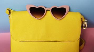 bolso amarillo y gafas de sol en forma de corazón sobre fondo rosa y azul foto