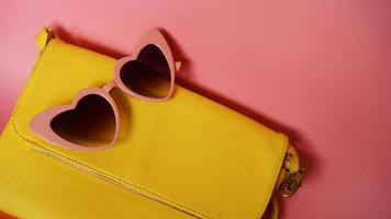 Yellow bag and heart-shaped sunglasses on pink background photo