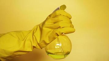 Mano en guante de goma amarillo sosteniendo spray de plástico foto