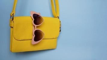 Bolsa amarilla y gafas de sol en forma de corazón sobre fondo azul. foto