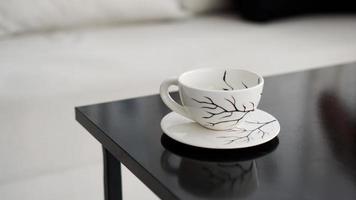 White coffee cup with a pattern of black branches on a black table photo