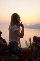 The girl looks at the sea sunset from a high point. Vertical photo