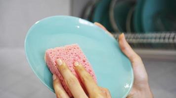 Blue plate with pink dish sponge in hand on blurred background photo