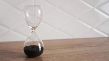 Reloj de arena de cristal con arena negra sobre mesa de madera foto