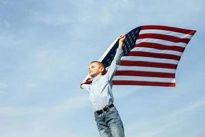 A little boy holds a flag of the United States against the sky