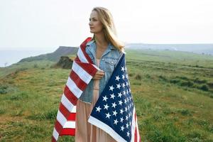 A girl in a coral dress and a denim jacket holds the flag of usa photo