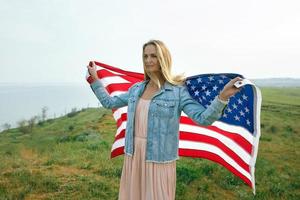 A girl in a coral dress and a denim jacket holds the flag of usa photo