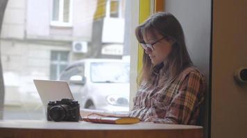 jovem de óculos trabalhando com laptop em uma cafeteria
