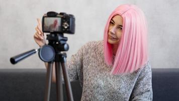 Happy girl blogger in pink wig in front of the camera on a tripod