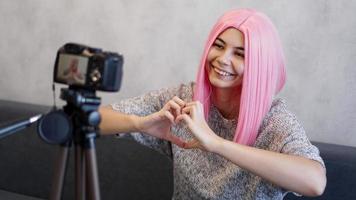 mujer mira a la cámara y muestra un signo de forma de corazón. chica con cabello rosado foto