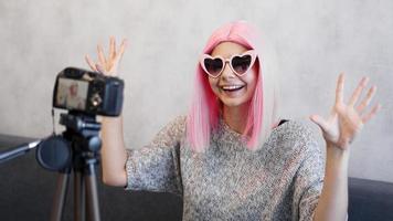 Happy girl blogger in pink wig in front of the camera on a tripod photo