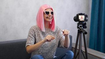 Happy girl blogger in pink wig in front of the camera on a tripod