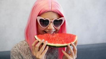 Woman with piece of watermelon. Woman wears pink wig and glasses photo
