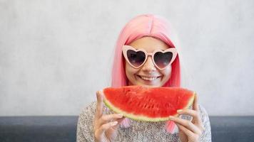 Woman with piece of watermelon. Woman wears pink wig and glasses photo