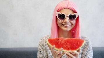 Woman with piece of watermelon. Woman wears pink wig and glasses photo