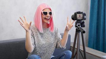 Happy girl blogger in pink wig in front of the camera on a tripod photo