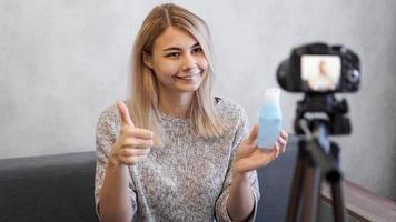 Blogger shows lotion for skin. Cheerful female blogger recording video photo