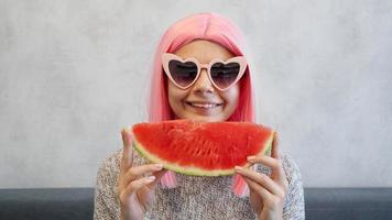 mujer con trozo de sandía. mujer usa peluca rosa foto