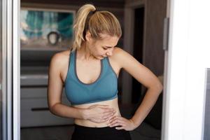 cerca de la mujer sosteniendo su vientre. dolor después del entrenamiento en casa. foto