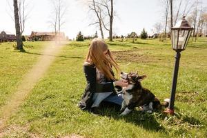 Mujer joven con gafas de sol rojas juega con su corgi foto