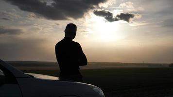 silueta del hombre parado cerca del coche y mirando una puesta de sol foto