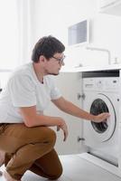 Young man putting clothes into washing machine photo