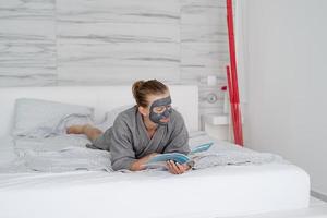 Mujer con mascarilla relajante acostado en la cama leyendo una revista