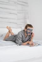 Mujer con mascarilla relajante acostado en la cama leyendo una revista