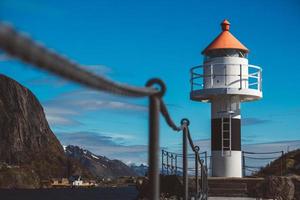 Lighthouse on the pier on the background of mountains and blue sky photo