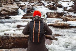 Hombre viajero de pie sobre una roca en el río y la cascada de la montaña foto