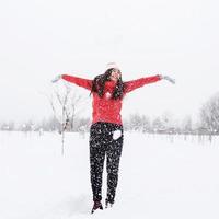 Joven mujer morena en suéter rojo jugando con la nieve en el parque foto