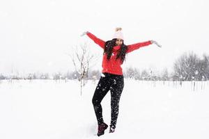 Joven mujer morena en suéter rojo jugando con la nieve en el parque foto