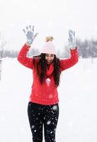 Joven mujer morena en suéter rojo jugando con la nieve en el parque foto