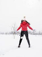 Joven morena despreocupada mujer en suéter rojo saltando en la nieve al aire libre foto