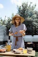 Young woman in summer hat grilling meat outdoors in the backyard photo