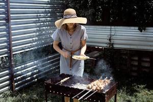 Mujer joven con sombrero de verano asar carne al aire libre en el patio trasero foto