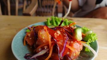 Slow motion closeup hand using chopsticks to eat salmon salad on table video