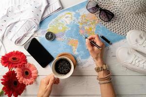 mujer de vista superior planeando un viaje, tomando café y dibujando en un mapa foto
