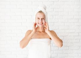 Happy smiling young woman applying scrub on her face and neck photo