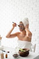 Mujer joven aplicar mascarilla facial spa en su rostro con un cepillo cosmético