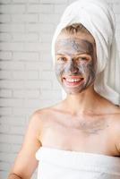 Feliz mujer sonriente con una mascarilla facial de arcilla en su rostro foto