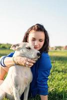 Hermosa joven sentada en la hierba abrazando a su perro en el parque foto