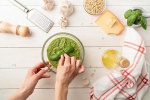 Woman hands putting fresh basil leaves on the top of the pesto bowl photo