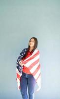 Hermosa joven envuelta en bandera americana sobre fondo azul. foto