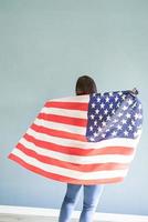 Woman with American flag on blue background, view from behind photo